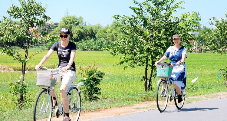 Zwei Personen fahren Fahrrad auf einer ländlichen Straße, umgeben von Grün.