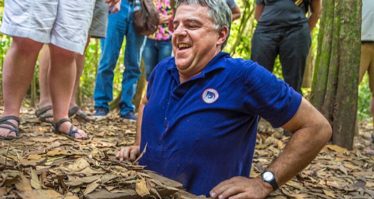 Person, die aus einem kleinen Eingang im Boden in einem bewaldeten Gebiet hervorkommt.