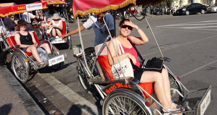 Toeristen rijden in traditionele fietstaxi's langs een drukke straat in Hanoi onder rode parasols.