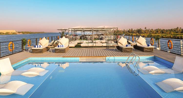 Deck of a Nile cruise ship with pool, sun loungers and river scenery during sunrise