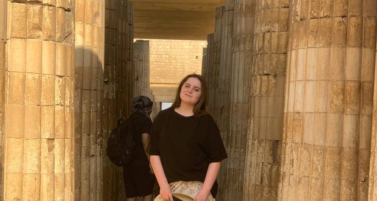 Young woman standing thoughtfully inside the sandstone colonnade of Saqqara at golden hour.