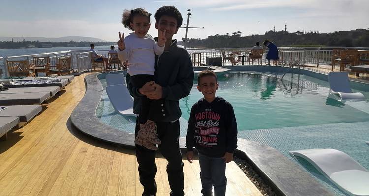 Un père et deux enfants posant près d'une piscine sur un bateau de croisière.