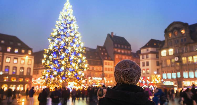 Visitor admires an enormous illuminated Christmas tree in a historic European square at twilight.