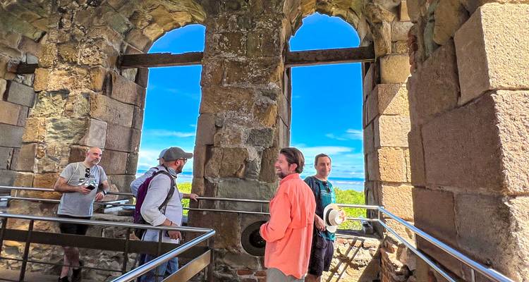 Turistas dentro de un edificio histórico con grandes ventanas que muestran una vista de la montaña.