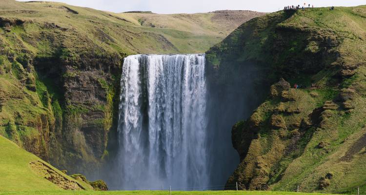 Profil latéral d'une haute cascade plongeant dans une vallée verdoyante étroite avec de minuscules silhouettes au-dessus