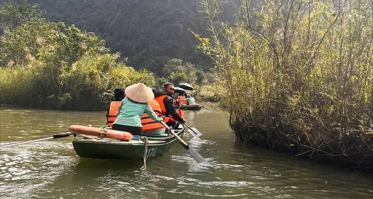 People rowing in traditional boats through a lush waterway.