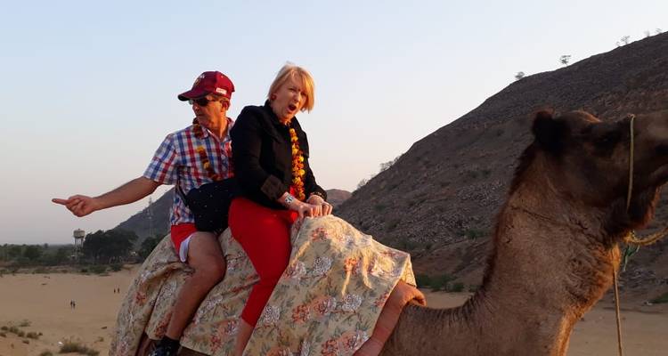 Mann und Frau reiten auf einem Kamel in einer trockenen Hügellandschaft der Wüste bei Sonnenuntergangslicht