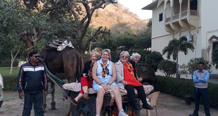 Gruppe von Reisenden, die auf einem Kamelwagen vor einem traditionellen indischen Wohnhaus posieren