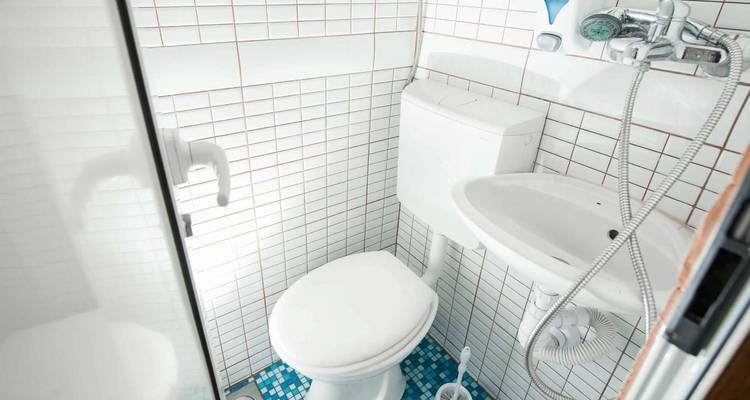 Salle de bain compacte avec carrelage blanc, toilettes et lavabo.