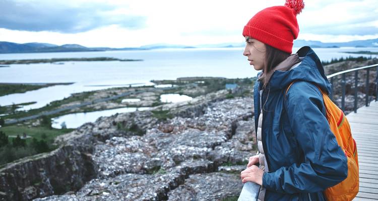 Person in red hat overlooking a dramatic landscape with water and cliffs.