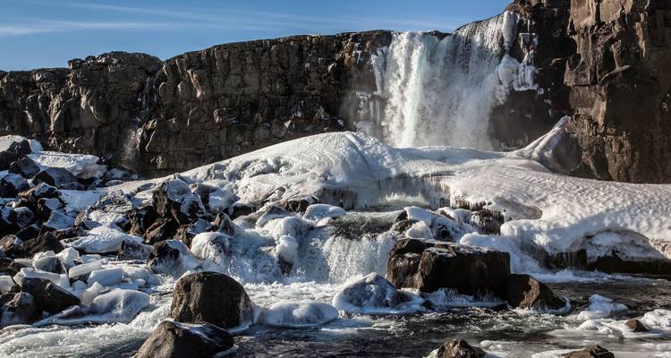 Frozen waterfall amidst rocky cliffs with flowing water.