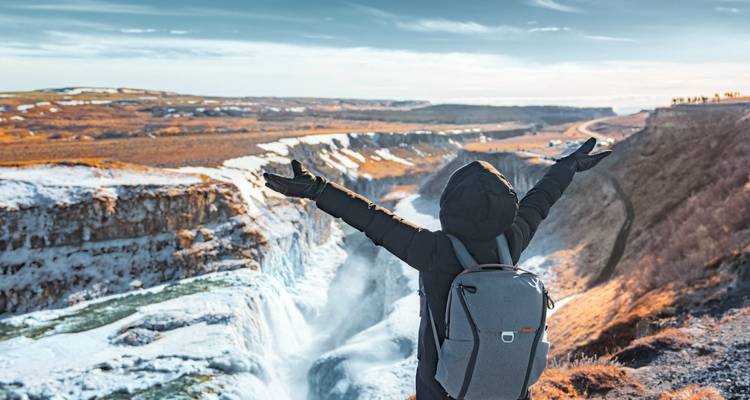 Person standing with arms open wide in front of Gullfoss waterfall.