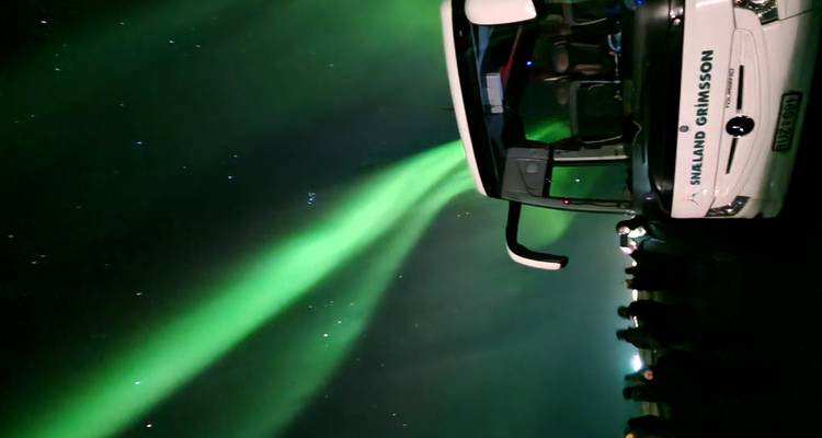 Bus under the northern lights at night, with people observing the sky.