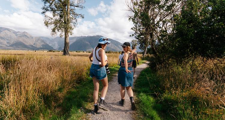 Deux personnes marchant sur un sentier pittoresque à travers des champs avec des montagnes en arrière-plan.