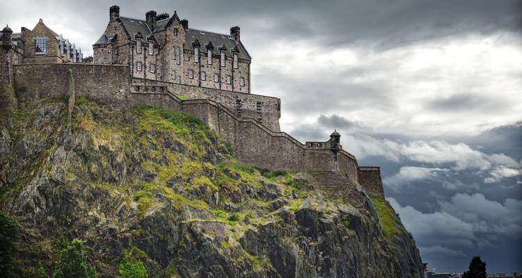 Edinburgh Castle thront über felsigen Klippen bei bewölktem Himmel.