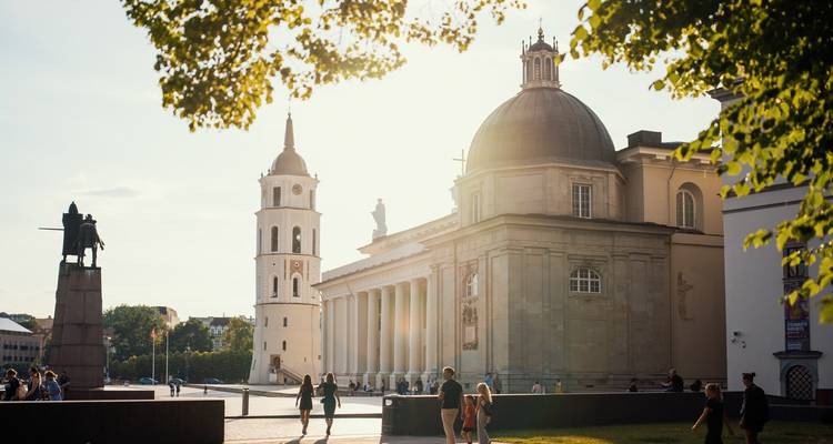 People walking near a historic bell tower and cathedral with columns.