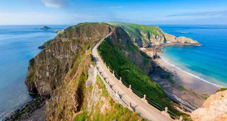 Panoramic aerial view of La Coupée, a narrow clifftop road joining two green headlands above turquoise sea.