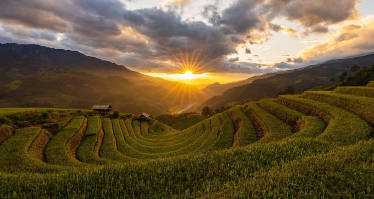 Atardecer sobre campos en terrazas con cielos dramáticos.