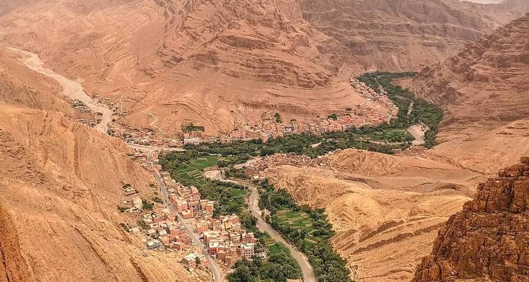 Vista aérea de un valle estrecho con un pueblo y un río serpenteando a través de él, rodeado de montañas escarpadas y marrones.