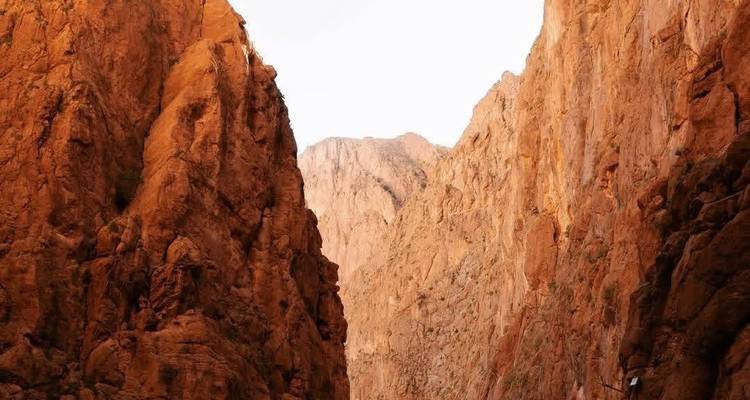 Los muros ocres empinados de la Garganta de Todra se elevan hacia un cielo blanco brillante creando un paso de cañón dramático.