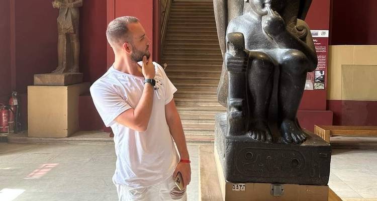 Man die poseert met een farao standbeeld in een museum.