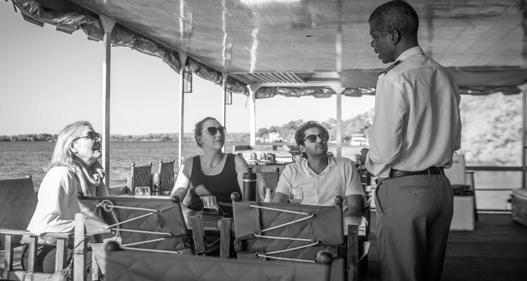A group of people sitting under a shaded area near the water, listening to a guide in a peaceful setting.