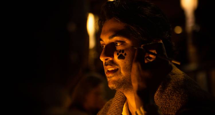 Man with face painting in a nighttime setting, possibly enjoying a cultural event.