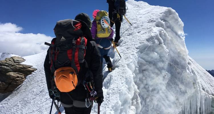 Groep klimmers die een besneeuwde top beklimmen.