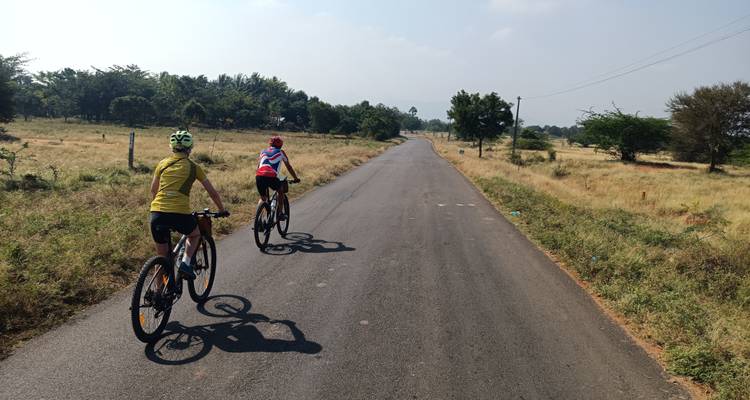 Twee fietsers rijden over een rechte, lege weg door het platteland.