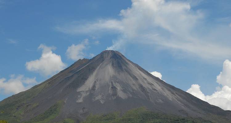 Le volcan Arenal conique s'élevant abruptement contre un ciel bleu éclatant avec un panache de fumée dérivant de son sommet.