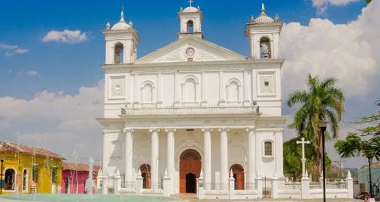 L'église blanche élégante aux deux clochers jumelés se dresse à la lisière d'une place coloniale sous un ciel bleu.
