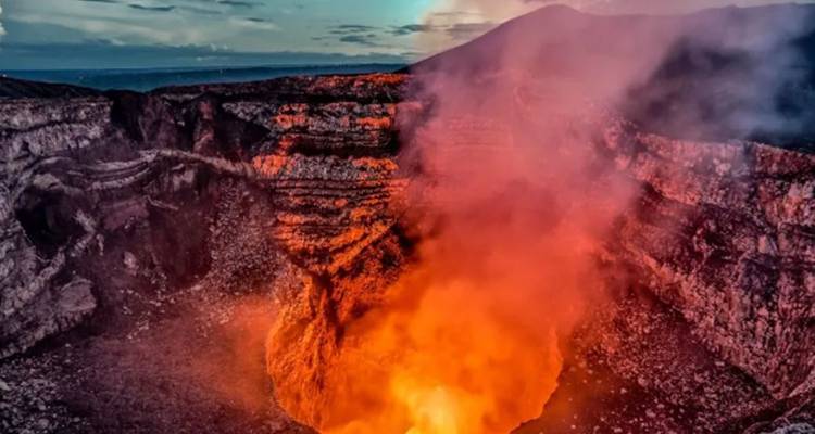 La lave orange ardente brille à l'intérieur du cratère fumant du volcan Masaya au crépuscule.