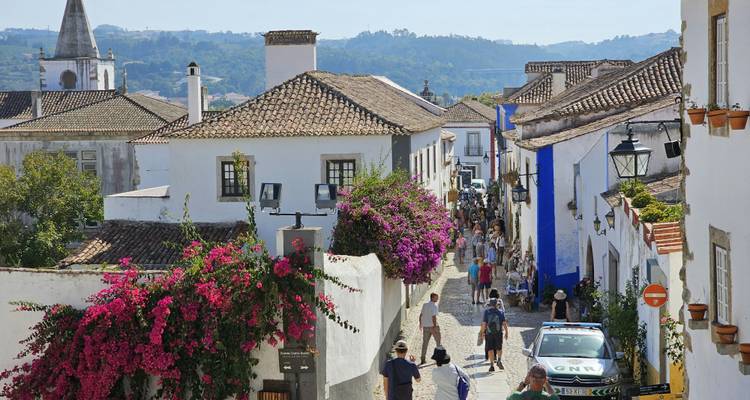 Charmante mittelalterliche Straße in Óbidos mit weißgetünchten Häusern, Blumen und spazierenden Besuchern