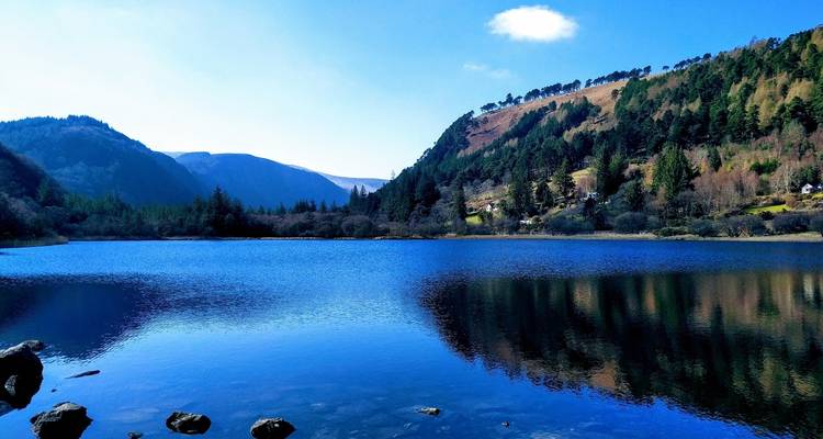 Crystal-blue mountain lake reflecting forested hills and distant peaks under a clear sky