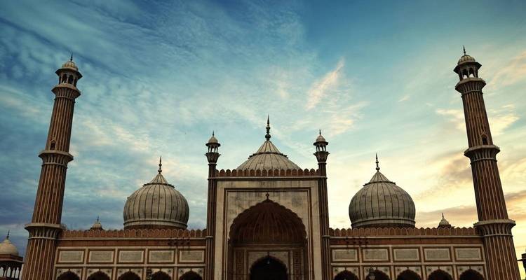 Grand Jama Masjid with three domes and soaring minarets framed by a dramatic twilight sky.
