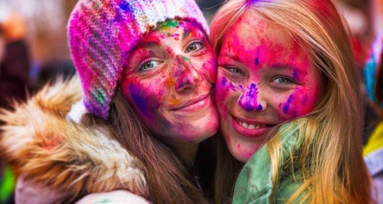 Two young women with colorful Holi powder smiling close together during festival celebrations.