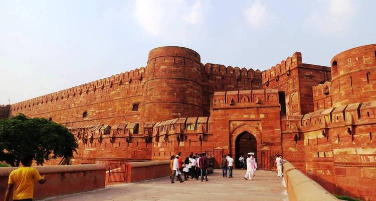 Tourists entering the imposing red sandstone walls of Agra Fort on a bright day.