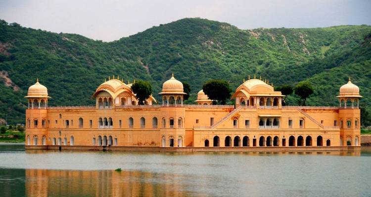 Serene Jal Mahal palace floating on calm lake waters with green hills behind.