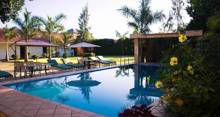 Ein ruhiger Poolbereich mit Sonnenliegen, umgeben von Palmen und Blumen.