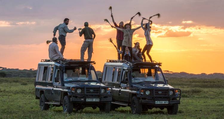 Gruppe von Menschen, die bei Sonnenuntergang auf Safari-Fahrzeugen stehen und tanzen.
