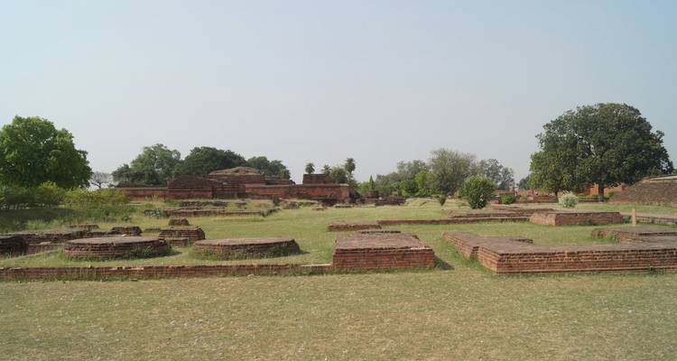 Ruinen alter Backsteinbauten und offene Grünflächen unter einem klaren Himmel.