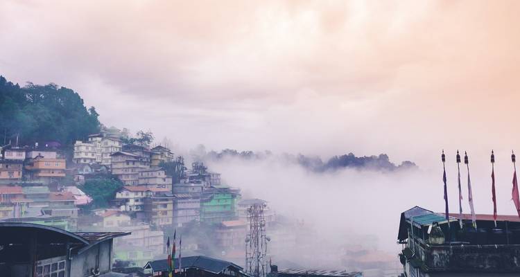 Neblige Stadtlandschaft auf einem Hügel mit bunten Gebäuden unter einem nebligen Himmel.