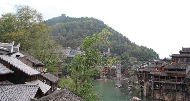 Blick auf eine historische chinesische Flussstadt, umgeben von Hügeln.