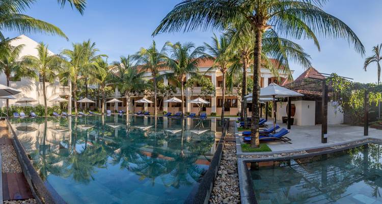 Een resortbad omringd door palmbomen en ligstoelen.