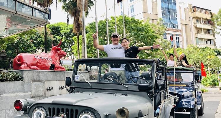 Menschen die genieten van een rit in open jeeps in een stedelijk gebied met een rode stier standbeeld en een modern gebouw.