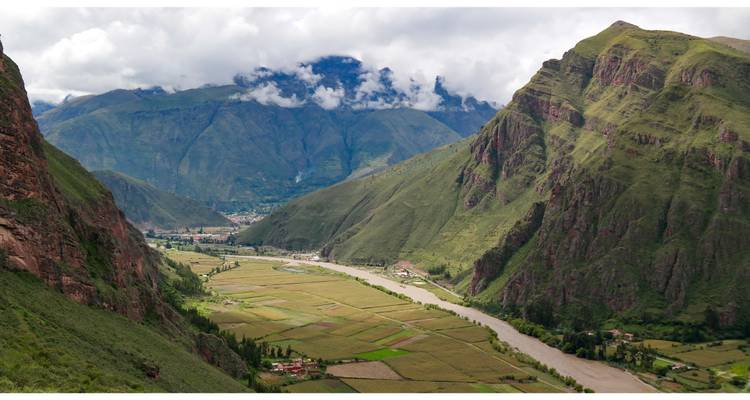 Uitgestrekte vallei met een rivier en bergen op de achtergrond.