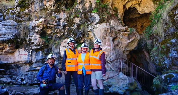 Groep van vier mensen met helmen en veiligheidsuitrusting voor een grotingang.
