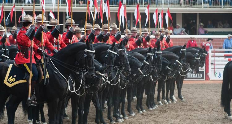 Line of Royal Canadian Mounted Police in red serge atop black horses performing a ceremonial ride in an arena.