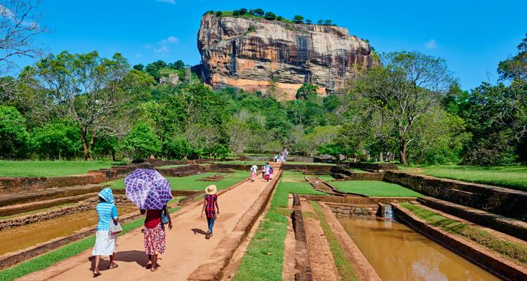 Pathway leading to the rock fortress of Sigiriya with people walking and lush greenery.