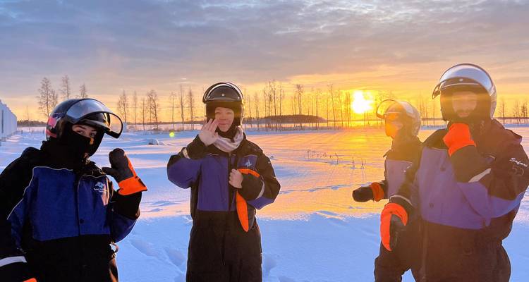 Group of people in winter gear waving at the camera with a sunset background.